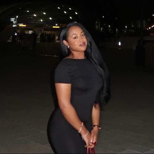 Woman in a black dress standing on a city street at night.